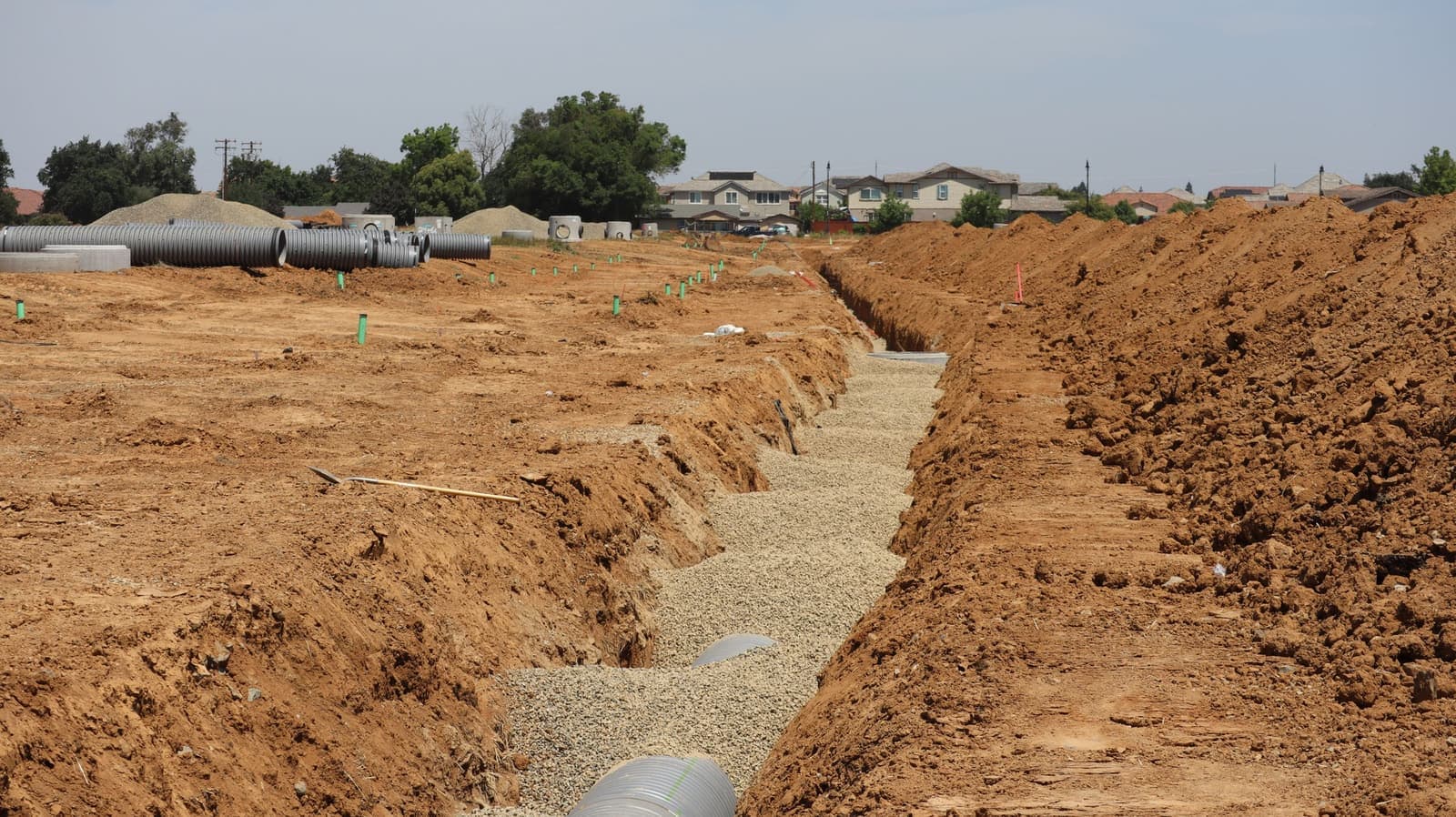 Long open trench with drain pipe in gravel beside a row of houses