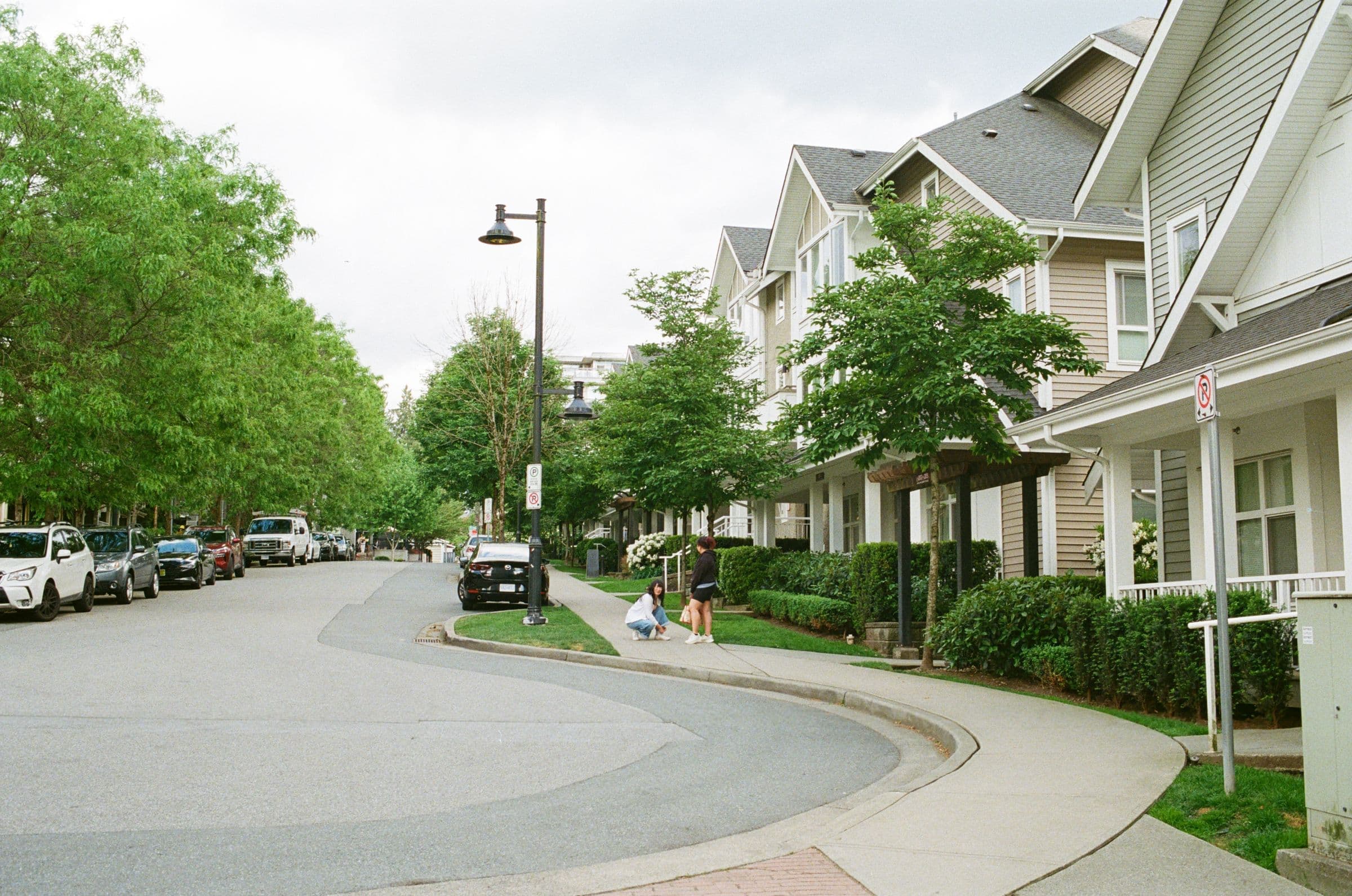 Curving residential street lined with newer townhouses and young trees
