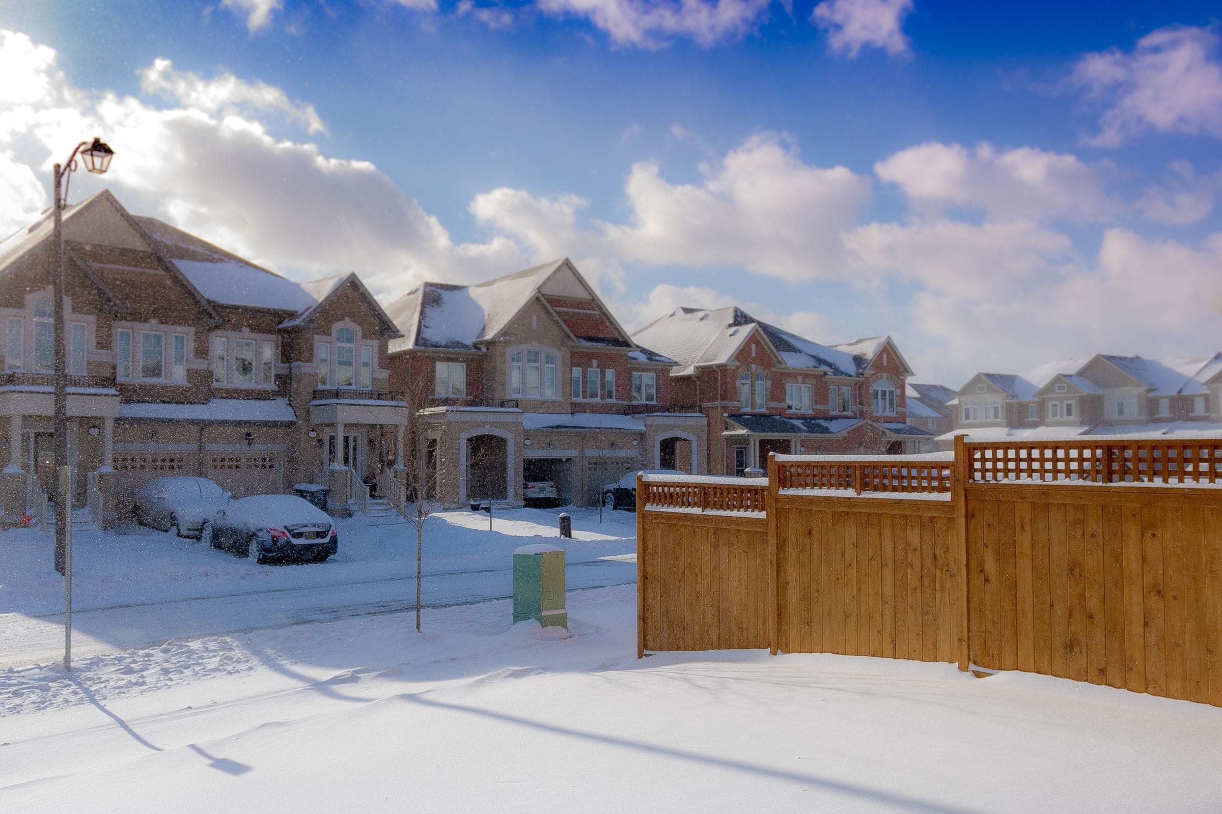 Row of newer brick two-storey houses behind a wood fence in winter snow
