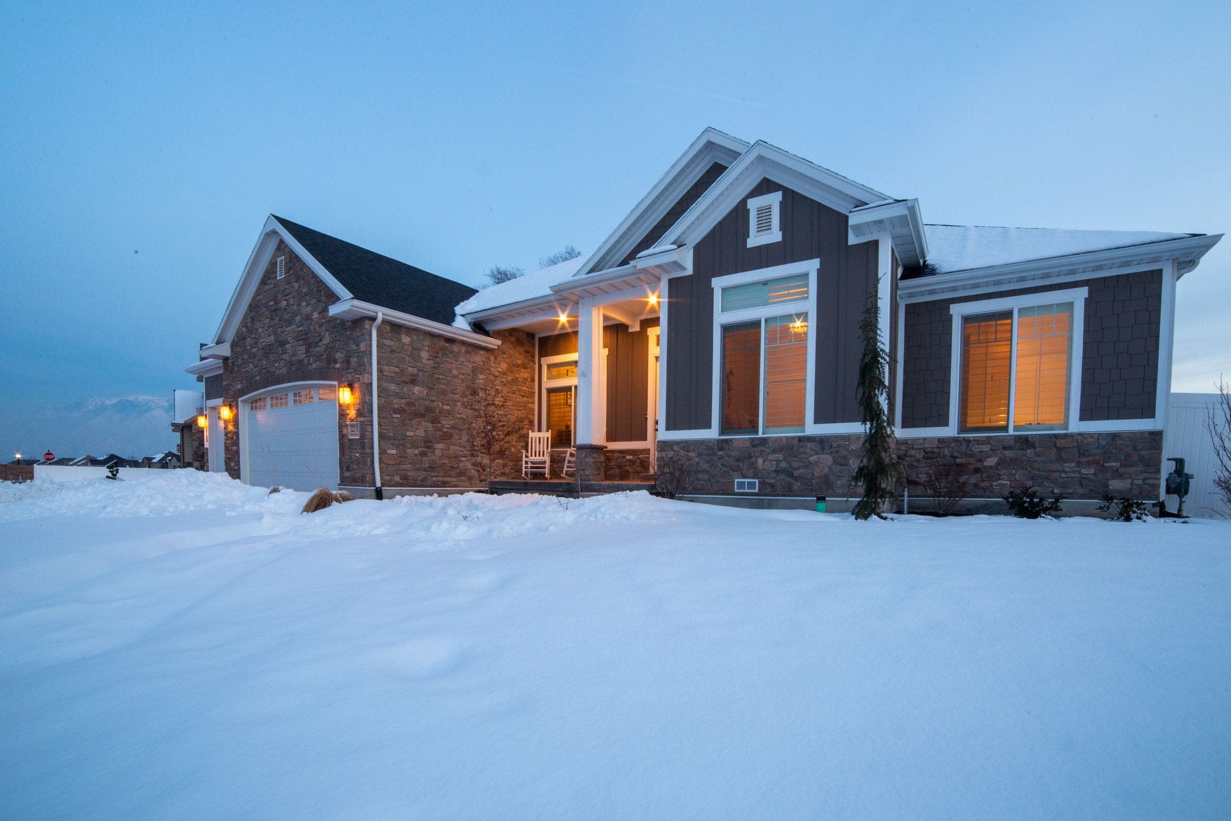 Large modern bungalow with a stone front and porch lights in deep snow