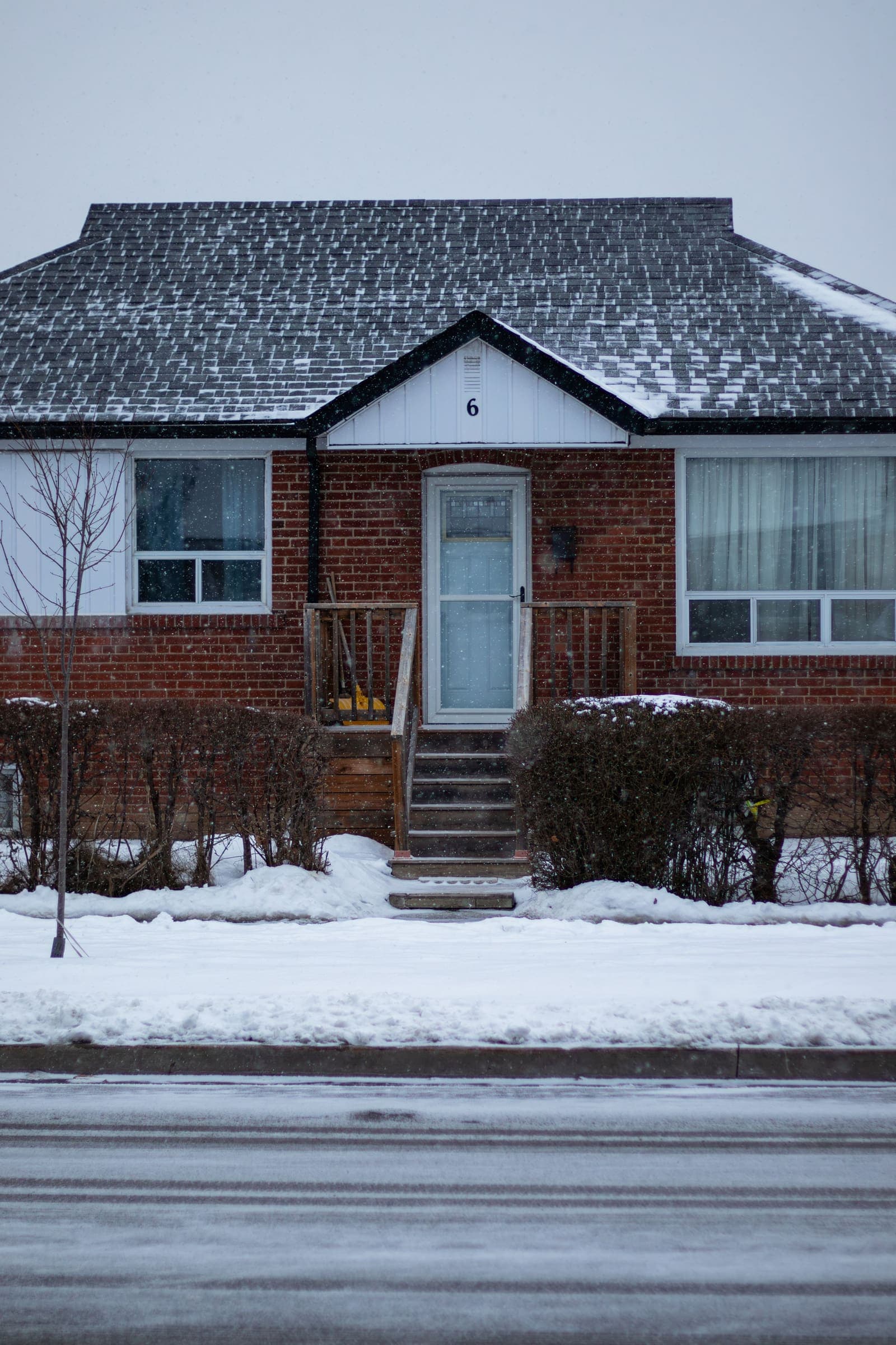 Red brick bungalow with front steps and snow along the walk