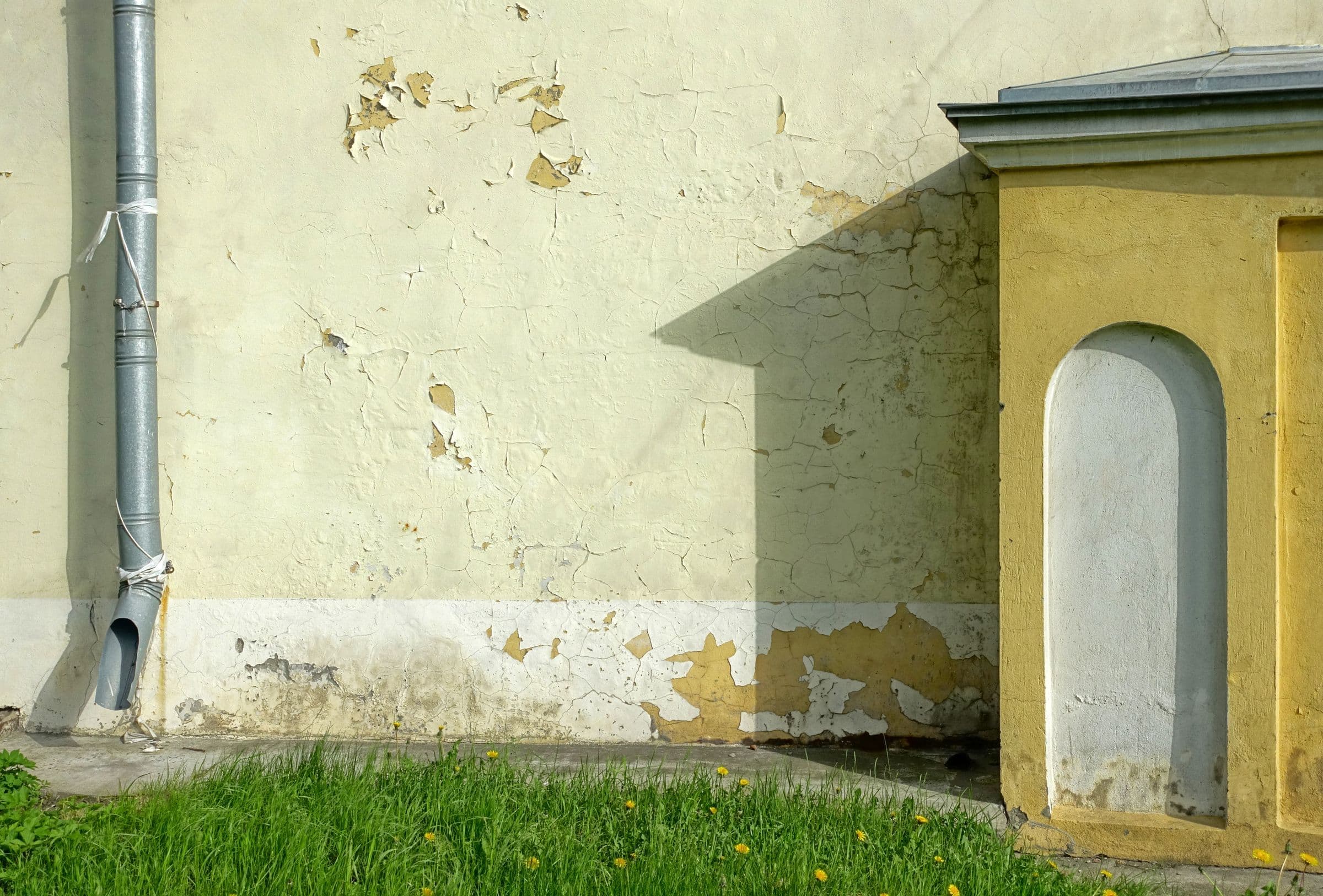 Damp, peeling foundation wall beside a downspout, a typical case for exterior basement waterproofing