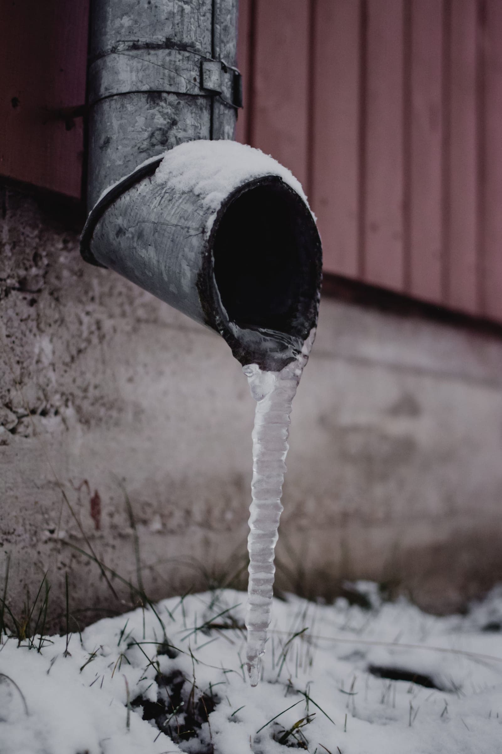Frozen discharge pipe beside a foundation in winter, the end of the line in a sump pump installation